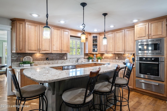 kitchen featuring sink, hanging light fixtures, a kitchen breakfast bar, stainless steel appliances, and light stone counters