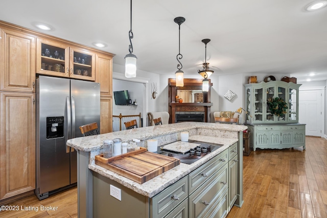 kitchen featuring light stone counters, hanging light fixtures, a center island, and stainless steel refrigerator with ice dispenser