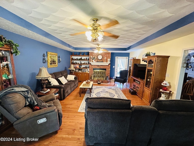 living room with ceiling fan, a textured ceiling, a fireplace, and light wood-type flooring