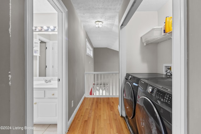 washroom with separate washer and dryer, sink, light hardwood / wood-style floors, and a textured ceiling