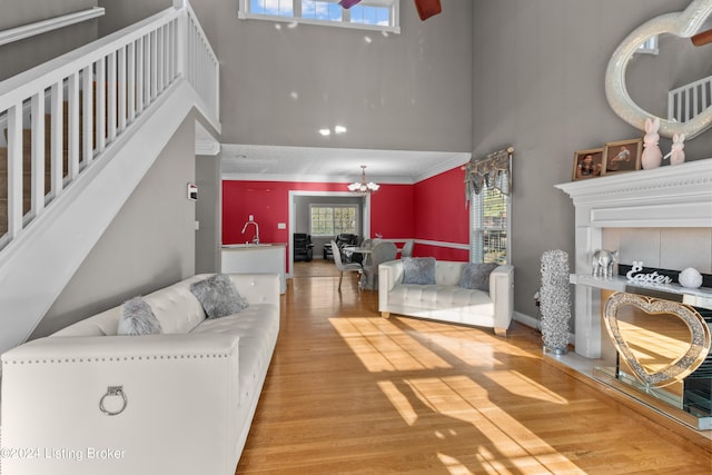 living room featuring sink, light wood-type flooring, a high ceiling, crown molding, and an inviting chandelier