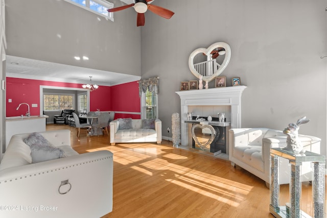 living room with a towering ceiling, ceiling fan with notable chandelier, a fireplace, sink, and light wood-type flooring