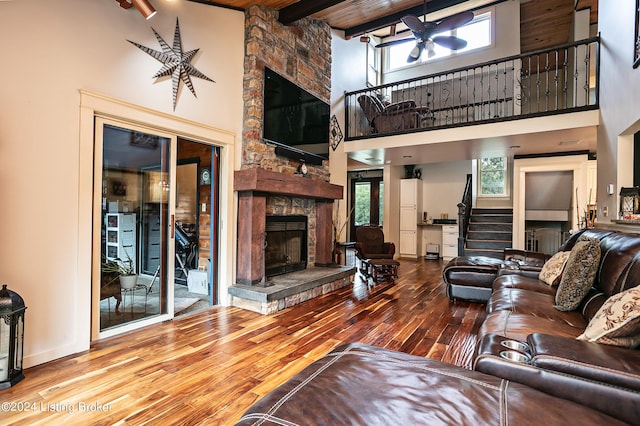 living room with a high ceiling, a stone fireplace, wooden ceiling, and beam ceiling