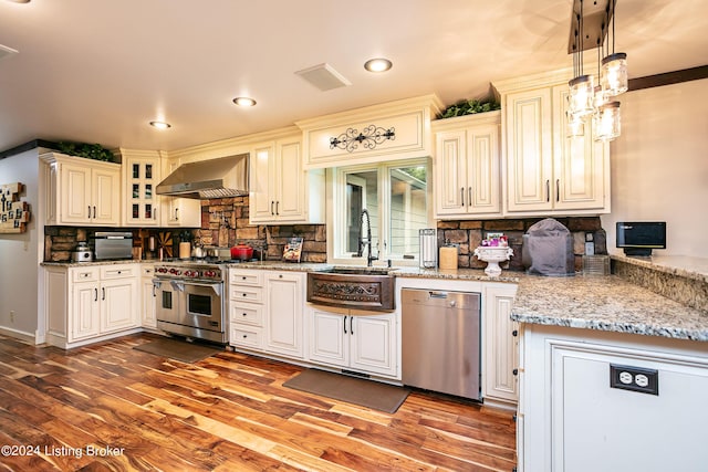 kitchen with appliances with stainless steel finishes, sink, hanging light fixtures, light stone countertops, and wall chimney range hood