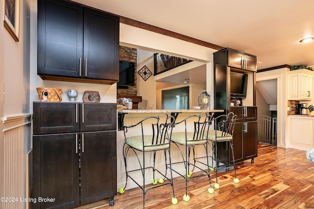 kitchen with crown molding, light stone countertops, a kitchen bar, kitchen peninsula, and light wood-type flooring