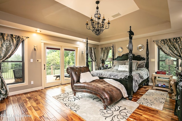 bedroom featuring an inviting chandelier, access to exterior, a tray ceiling, and wood-type flooring