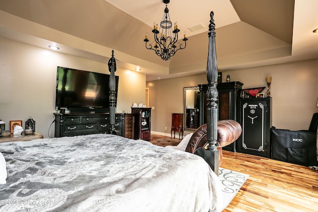 bedroom with a tray ceiling, a chandelier, and light hardwood / wood-style floors