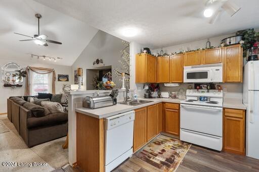 kitchen with vaulted ceiling, white appliances, kitchen peninsula, and sink