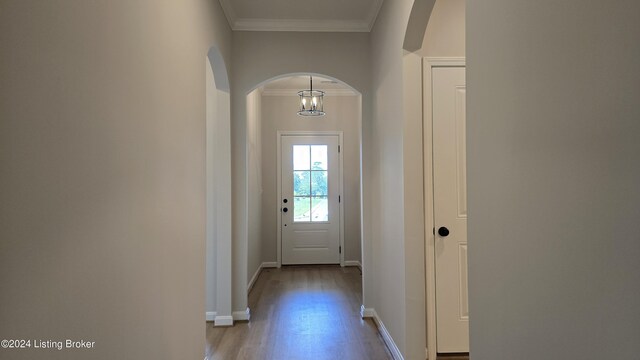 doorway to outside featuring an inviting chandelier, ornamental molding, and light hardwood / wood-style flooring