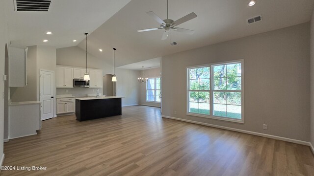 kitchen featuring ceiling fan with notable chandelier, pendant lighting, white cabinets, light hardwood / wood-style floors, and a center island with sink