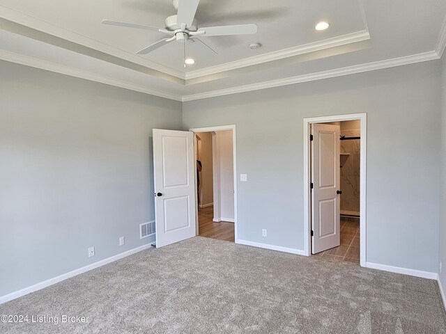 unfurnished bedroom with ceiling fan, light colored carpet, crown molding, and a tray ceiling