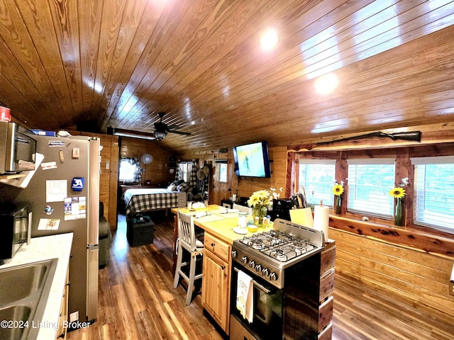 kitchen with lofted ceiling, appliances with stainless steel finishes, light wood-style floors, a sink, and wooden walls