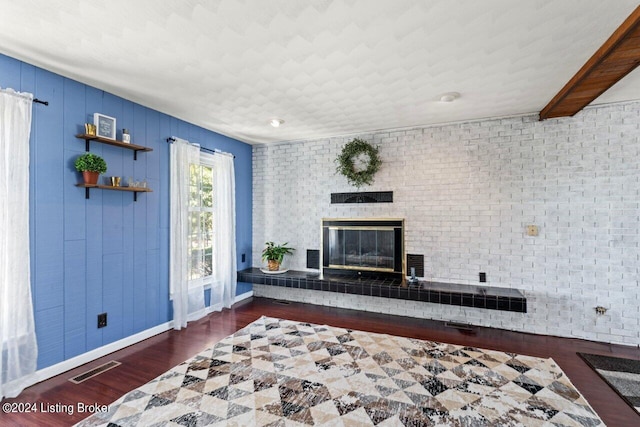 unfurnished living room with a fireplace, brick wall, and dark hardwood / wood-style floors