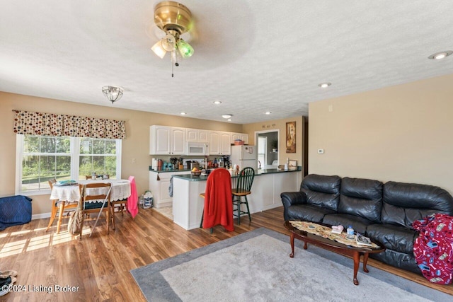 living room with a textured ceiling, ceiling fan, and light wood-type flooring