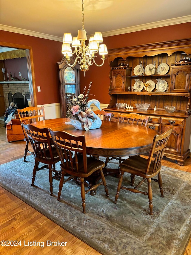 dining room with crown molding, a brick fireplace, a notable chandelier, and light hardwood / wood-style floors