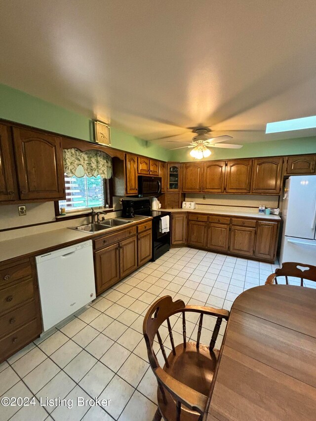 kitchen featuring white appliances, sink, a skylight, light tile patterned flooring, and ceiling fan