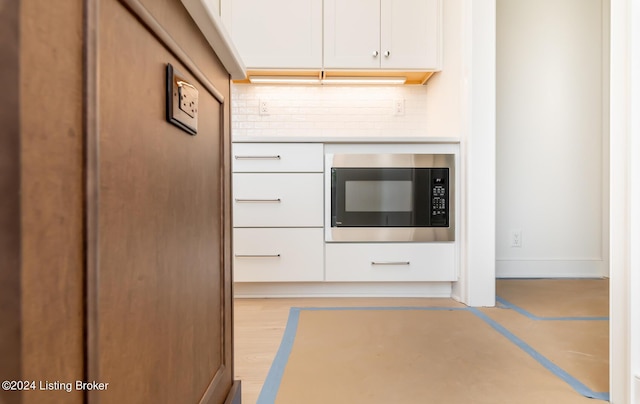 kitchen featuring built in microwave, backsplash, and white cabinetry