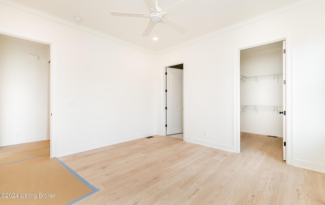 unfurnished bedroom with ceiling fan, ornamental molding, a spacious closet, a closet, and light wood-type flooring