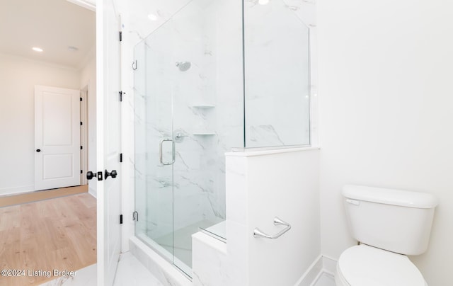 bathroom with wood-type flooring, a shower with door, and toilet