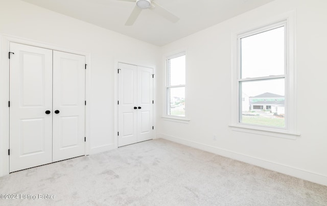 unfurnished bedroom with multiple closets, ceiling fan, and light carpet