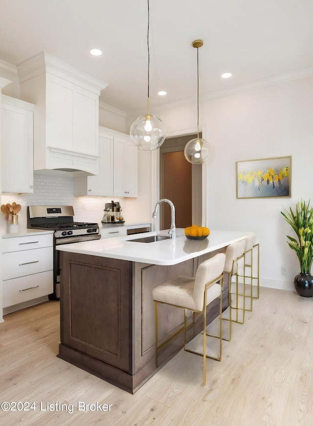 kitchen featuring white cabinetry, stainless steel gas range oven, sink, and an island with sink