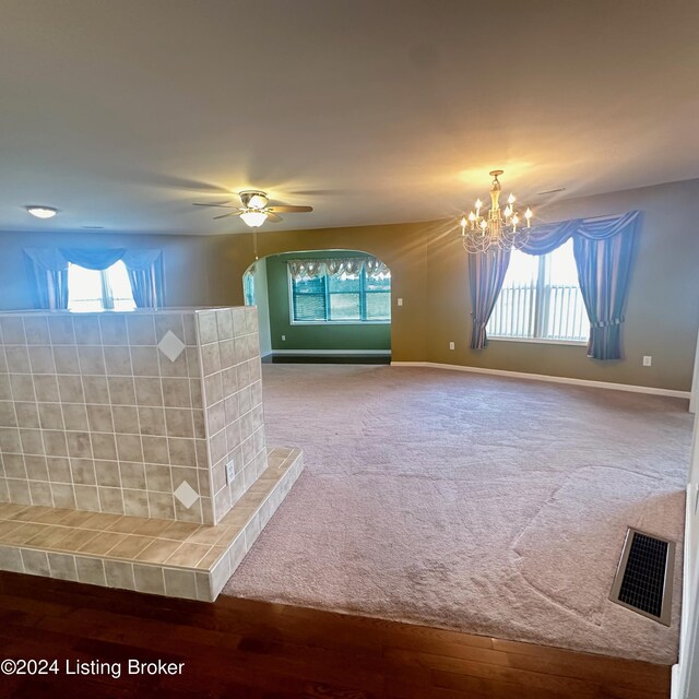 unfurnished living room with ceiling fan with notable chandelier, a healthy amount of sunlight, and hardwood / wood-style flooring