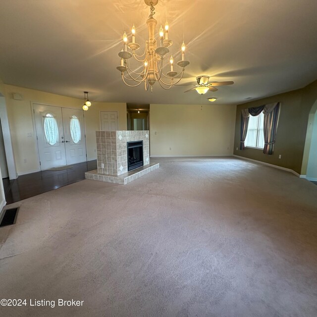 unfurnished living room featuring a fireplace, carpet, and ceiling fan with notable chandelier