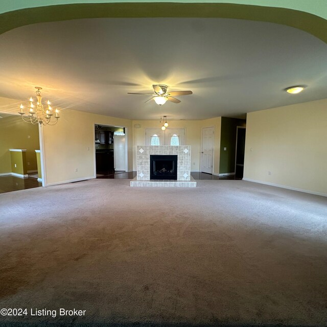 unfurnished living room featuring carpet, ceiling fan with notable chandelier, and a tile fireplace