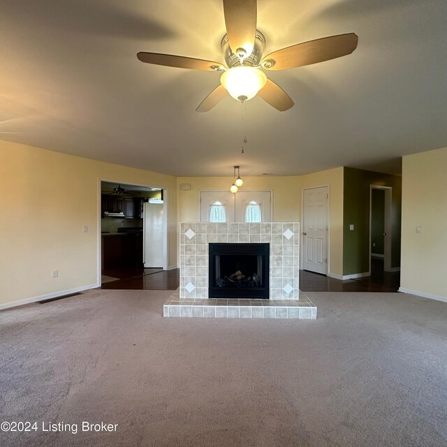 unfurnished living room featuring ceiling fan, a tiled fireplace, and dark carpet