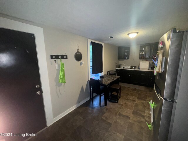 kitchen with dark cabinets, baseboards, light countertops, freestanding refrigerator, and glass insert cabinets