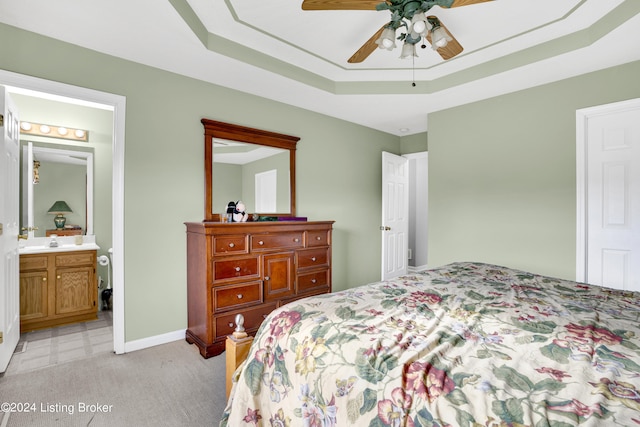 bedroom with light carpet, a raised ceiling, ceiling fan, and ensuite bath