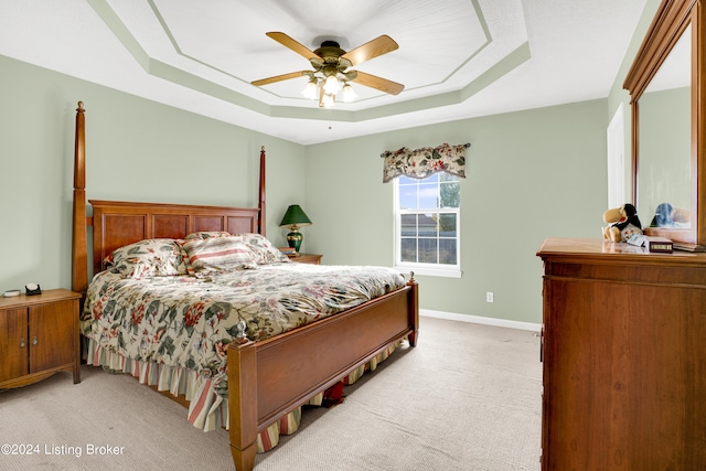 bedroom featuring a raised ceiling, light colored carpet, and ceiling fan