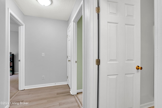 corridor with a textured ceiling and light wood-type flooring