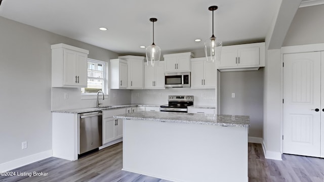 kitchen with appliances with stainless steel finishes, hanging light fixtures, a center island, light stone counters, and white cabinets