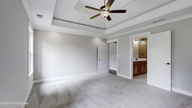 unfurnished bedroom with ornamental molding, light colored carpet, ensuite bath, and a tray ceiling