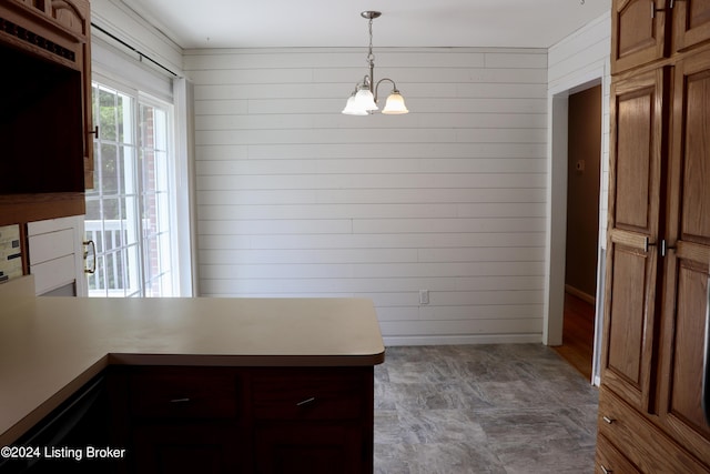 kitchen featuring hanging light fixtures, kitchen peninsula, a notable chandelier, and wood walls