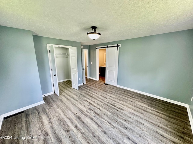 unfurnished bedroom featuring a textured ceiling, a barn door, a closet, and light hardwood / wood-style flooring