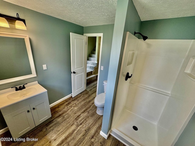 bathroom featuring vanity, wood-type flooring, a textured ceiling, a shower, and toilet