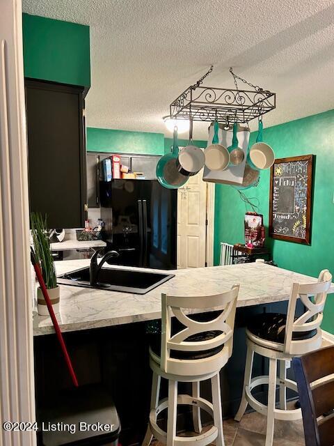 kitchen with tile patterned flooring, a textured ceiling, black fridge, a kitchen breakfast bar, and sink