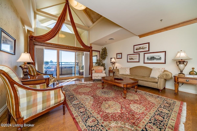 living room featuring wood finished floors, visible vents, baseboards, vaulted ceiling, and ornamental molding