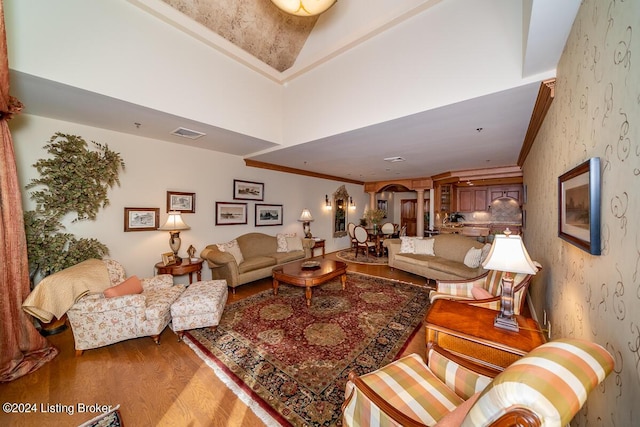 living area with arched walkways, visible vents, wallpapered walls, and wood finished floors