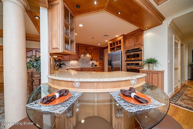 kitchen with light stone counters, stainless steel appliances, tasteful backsplash, a sink, and ornate columns