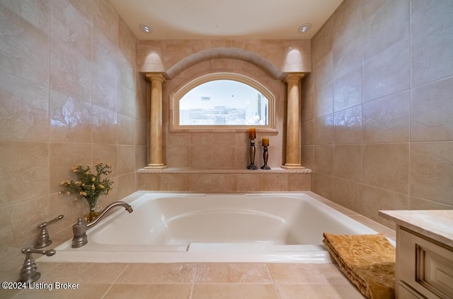 bathroom with a garden tub, ornate columns, tile walls, and vanity