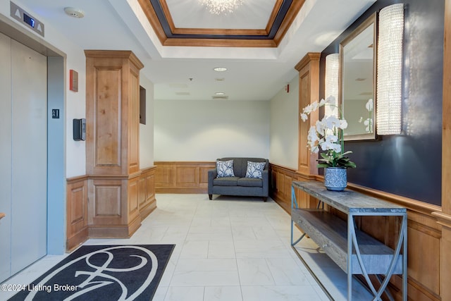 interior space featuring a tray ceiling, marble finish floor, crown molding, elevator, and wainscoting