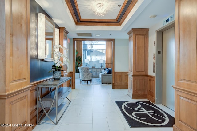 entrance foyer featuring decorative columns, a raised ceiling, wainscoting, elevator, and ornamental molding