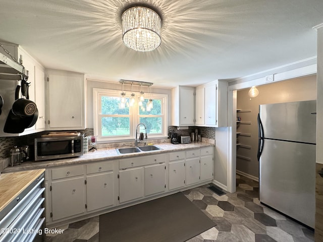 kitchen featuring sink, white cabinets, a chandelier, backsplash, and stainless steel appliances