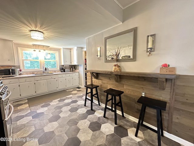 kitchen with sink, white cabinets, decorative backsplash, ornamental molding, and range