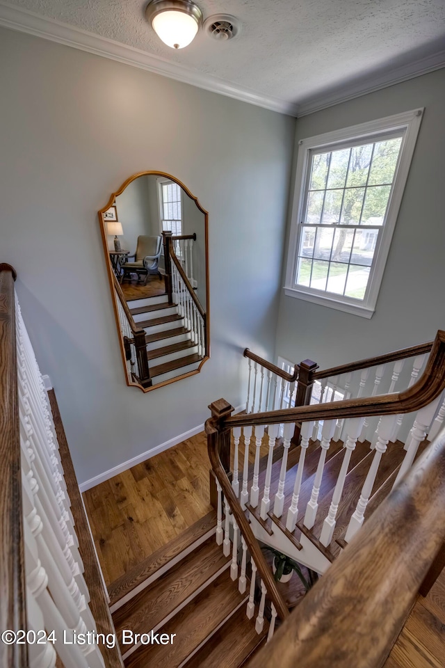 staircase with hardwood / wood-style flooring, crown molding, and a textured ceiling