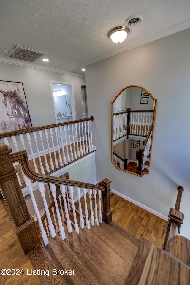 stairway with a textured ceiling, ornamental molding, and wood-type flooring