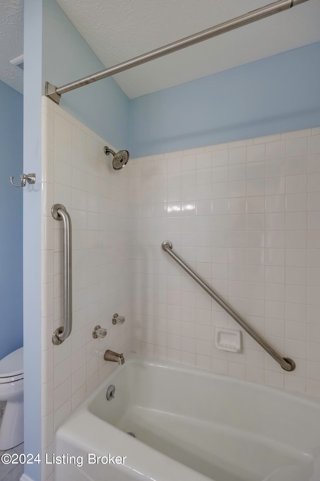 bathroom with a textured ceiling, toilet, and tiled shower / bath